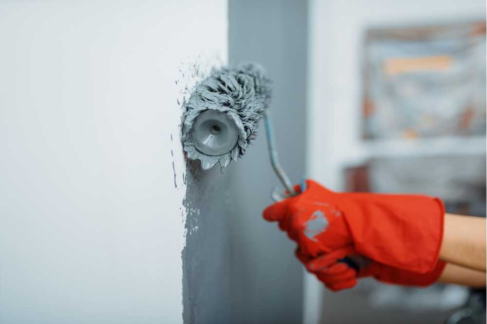 A person in red gloves expertly tackles interior painting, transforming a wall to a sleek gray with a paint roller.